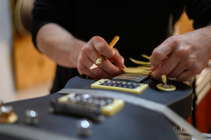 A person adjusts guitar strings with precision, focusing on the intricate details of a black electric guitar. The atmosphere conveys attentiveness.