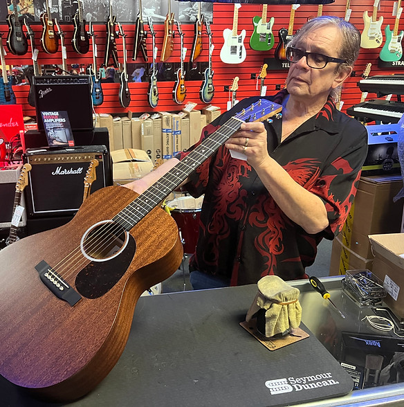 A person inspects an acoustic guitar in a vibrant music store filled with various guitars on red walls. The scene conveys an atmosphere of passion for music.